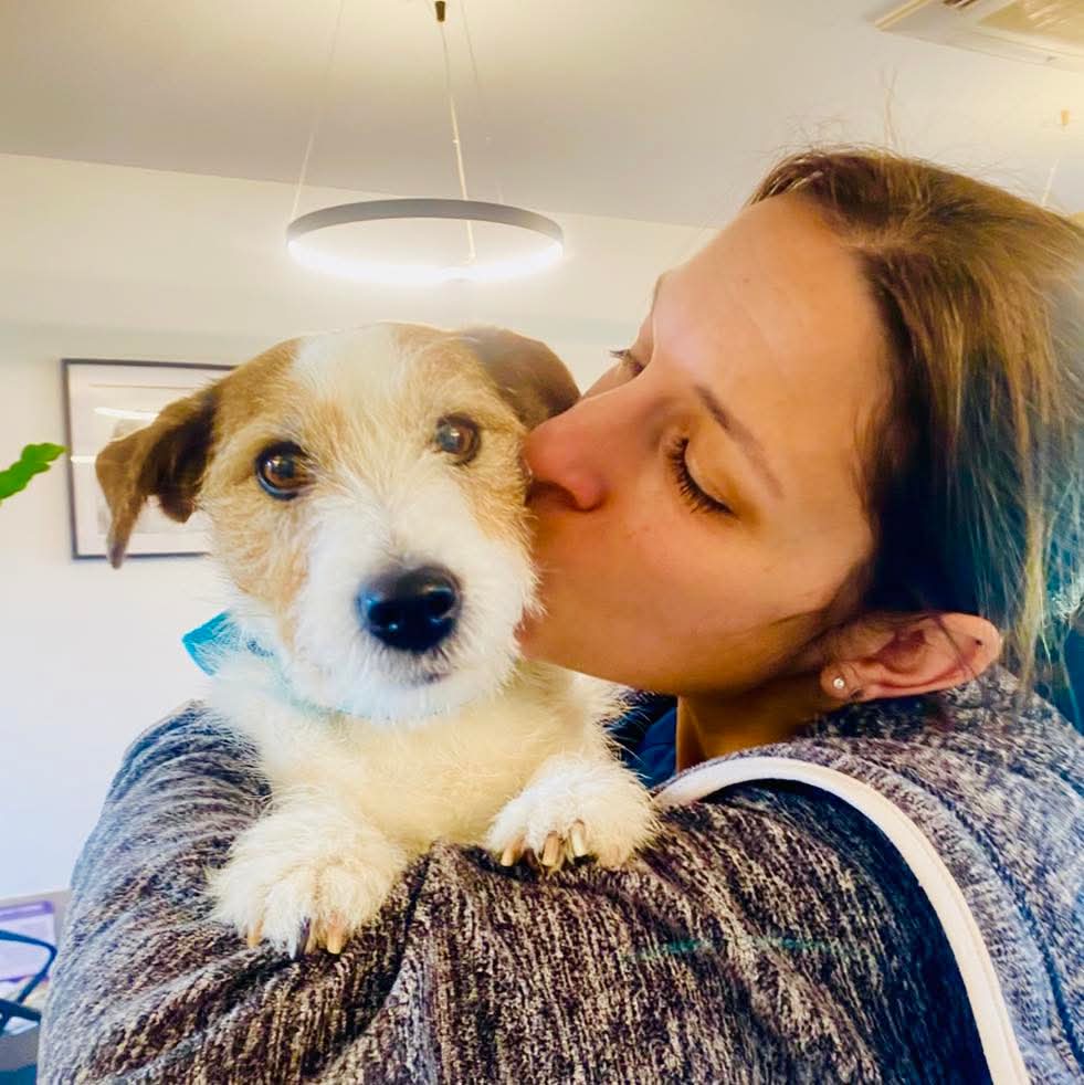 Femme embrassant un petit chien blanc et marron, qu'elle tient dans ses bras.